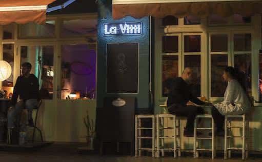 Vista nocturna de la entrada de La Vitti con clientes en la barra exterior