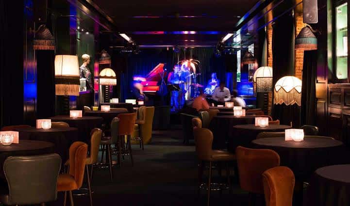 Interior del Jungle Jazz Club con escenario iluminado y mesas de clientes