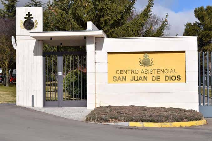 Entrada con letrero institucional del Centro Asistencial San Juan de Dios, rodeada de vegetación y portón metálico