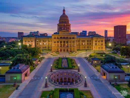 Fachada frontal del Capitolio de Texas al atardecer con cielo colorido y jardines bien cuidados
