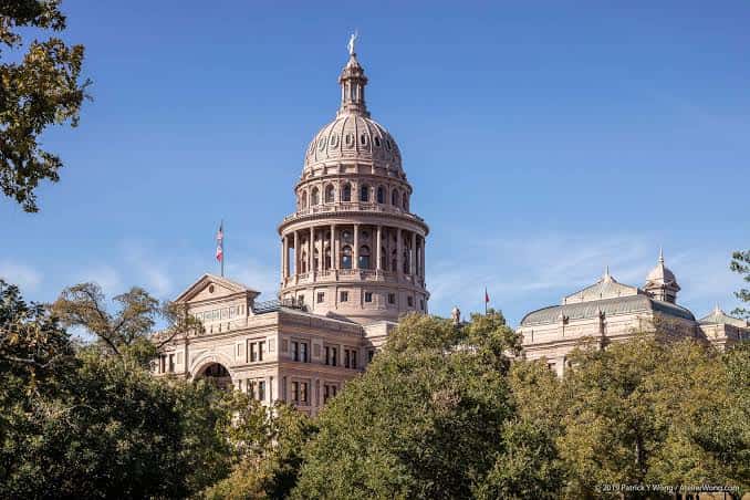 Cúpula del Capitolio de Texas en un día soleado, rodeada de árboles verdes y cielo azul
