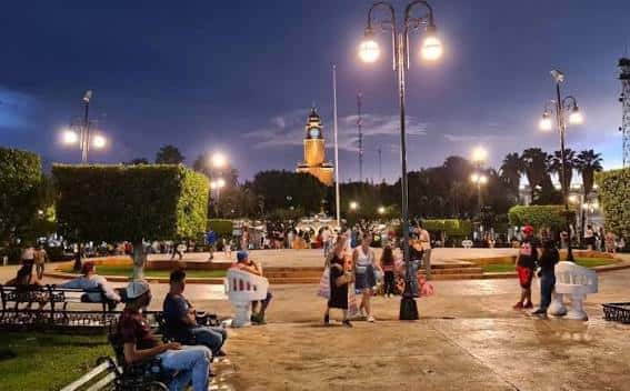 Plaza Grande de Mérida por la noche con personas disfrutando del parque y el reloj iluminado