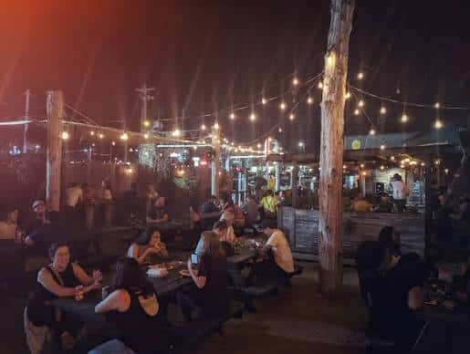 Ambiente festivo en el patio del Buzz Mill con mesas de picnic y luces decorativas