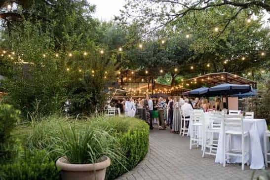Evento al aire libre en el patio con luces de hadas, mesas blancas y ambiente festivo