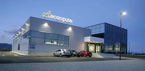 Sede central de Ecomputer en Huesca, edificio moderno con fachada metálica y logotipo iluminado al atardecer