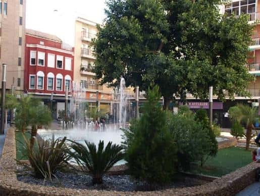 Fuente en la plaza rodeada de vegetación y edificios