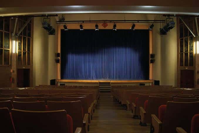 Interior del auditorio con butacas rojas y cortina azul en el escenario