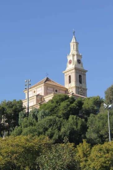 Torre del campanario del santuario sobre un fondo de cielo azul y vegetación