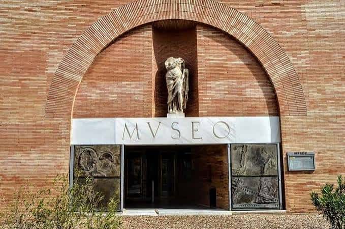 Entrada principal del museo con arco de ladrillo y estatua clásica sobre el letrero 'MVSEO'