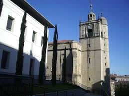 Torre de la iglesia de San Juan Bautista con cipreses altos y cielo despejado
