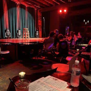 Escenario de comedia con público sentado en mesas y luces rojas