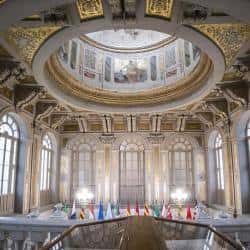 Interior del salón de actos con cúpula decorada y banderas internacionales en el escenario