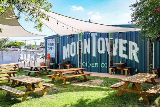 Área al aire libre con mesas de picnic y toldos en Moontower Cider Co