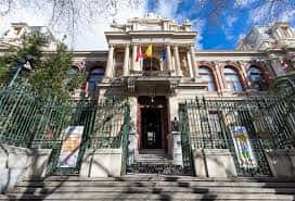 Entrada principal con escalinata, verja verde y banderas en el balcón