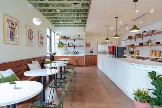Interior moderno del café con mesas redondas, sillas verdes y decoración minimalista