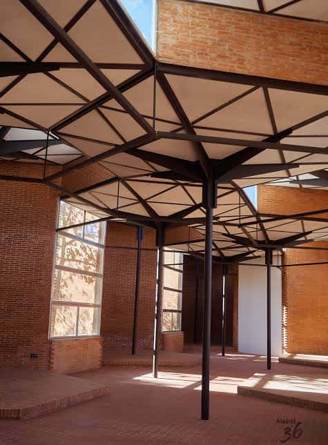 Espacio interior amplio del pabellón con techos de diseño geométrico y paredes de ladrillo bajo luz natural