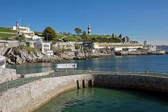 Vista panorámica del West Hoe Pier con el faro y edificios costeros bajo un cielo despejado