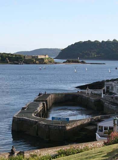 Vista del West Hoe Pier con veleros en el mar y colinas verdes al fondo