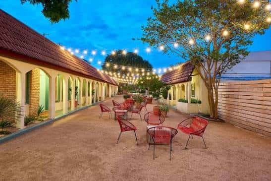 Patio exterior del Austin Motel con mesas y sillas rojas bajo luces de cadena al atardecer
