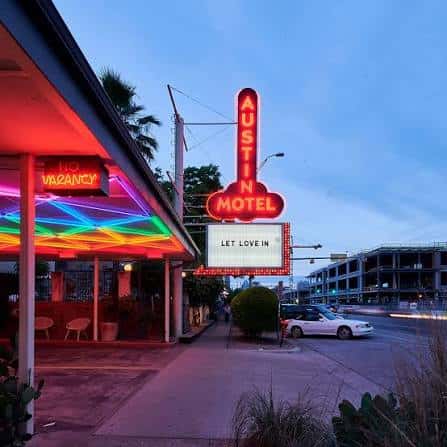 Fachada del Austin Motel con letrero de neón rojo y cartel de 'Let Love In' en la noche