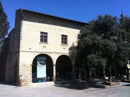 Fachada diurna del edificio histórico con arcos y árboles en la plaza