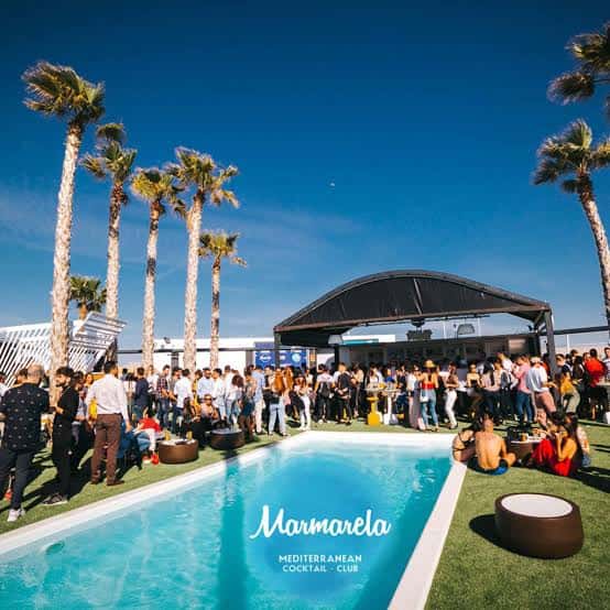 Ambiente festivo junto a la piscina con palmeras y público disfrutando del día