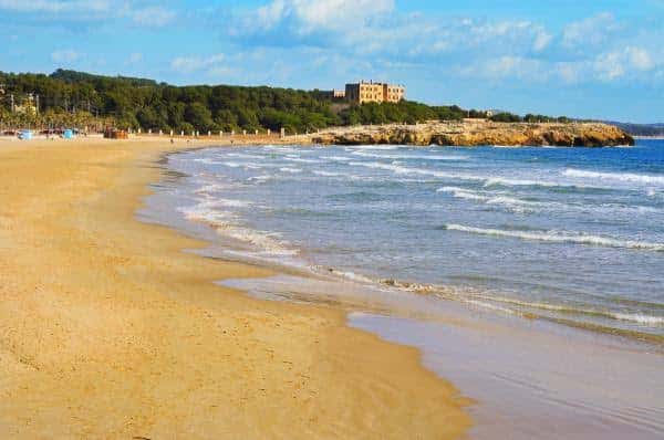 Playa de la Arrabassada con arena dorada y olas suaves bajo un cielo azul