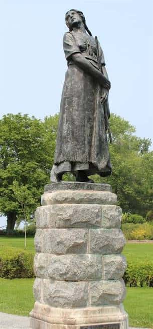 Estatua de una mujer acadiana en un parque con árboles verdes