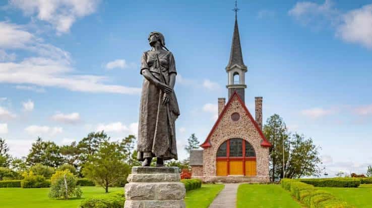 Estatua acadiana frente a una iglesia histórica con cielo azul