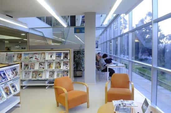 Interior luminoso de la biblioteca con zona de lectura y estanterías de prensa