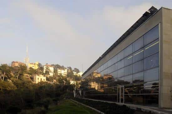 Vista exterior de la Biblioteca Collserola con fachada de cristal y el Tibidabo al fondo
