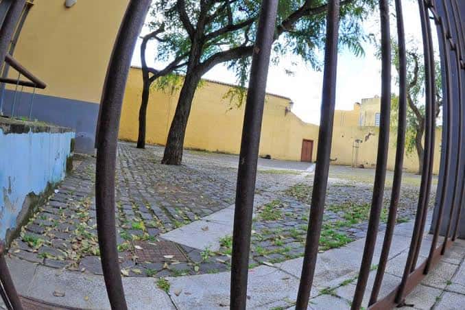 Vista de la plaza a través de una reja con árboles y edificio amarillo