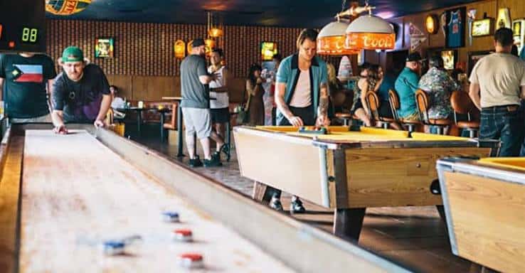 Interior del bar mostrando mesas de shuffleboard y ambiente social