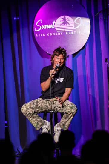 Comediante masculino actuando en el escenario con el logo del club al fondo