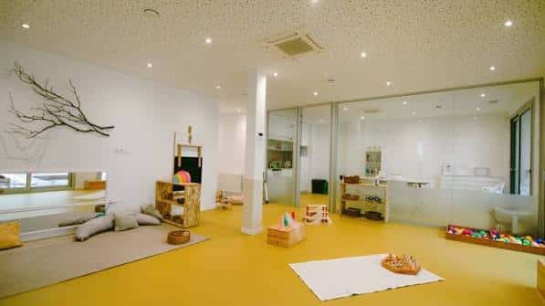 Sala de juego interior con suelo amarillo y mobiliario pedagógico