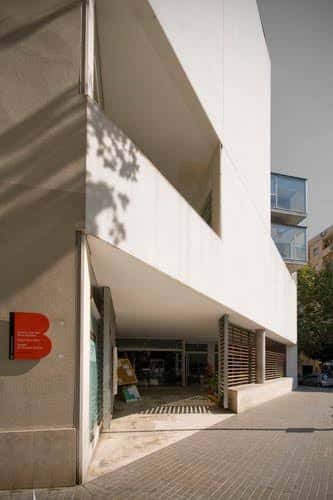 Entrada principal del edificio con diseño arquitectónico moderno y sombra de árbol