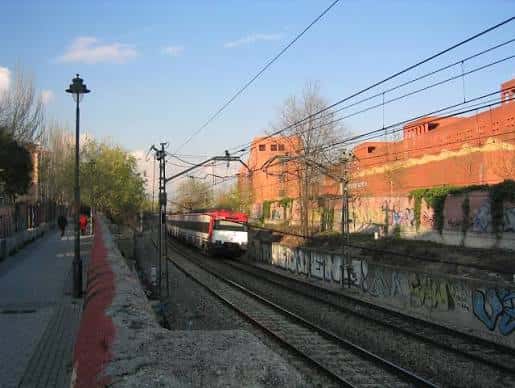Vista de la estación de cercanías de San Nicasio con tren en los vías y entorno urbano