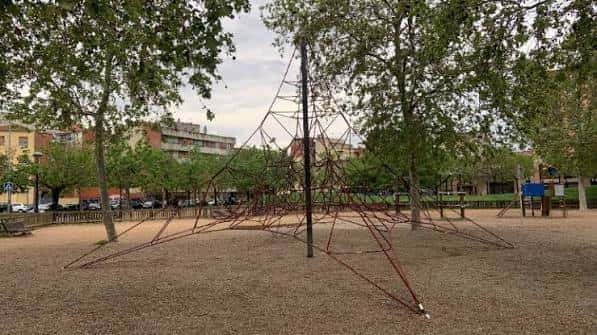 Área de juegos infantiles en la Plaça Fidel Aguilar con estructura de escalada y zona de arena