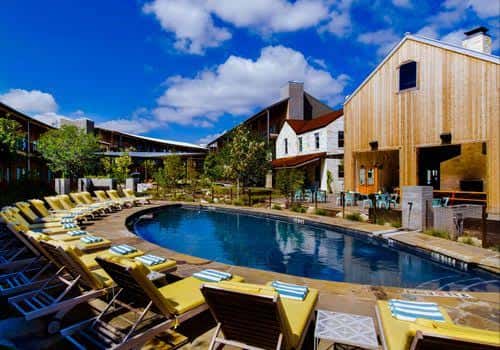 Piscina exterior con tumbonas y edificios de madera bajo cielo azul