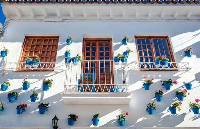 Fachada tradicional con ventanas de madera y macetas azules colgantes