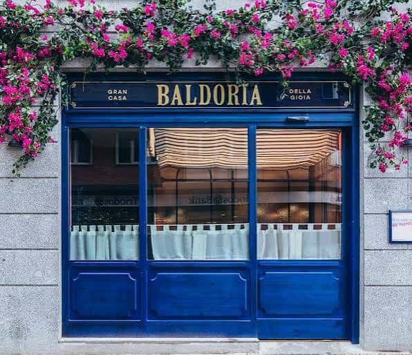 Fachada exterior de Baldoria con flores y letrero azul
