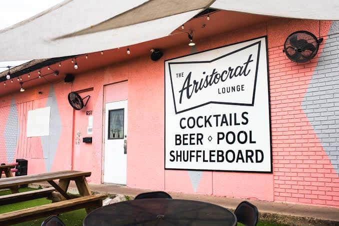 Fachada exterior del The Aristocrat Lounge con su distintiva pared rosa y letrero de neón