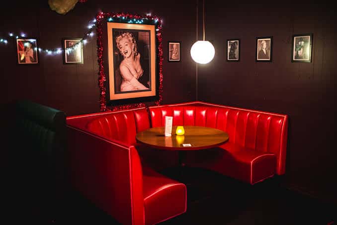 Interior del lounge con booth rojo, mesa redonda y retrato de Marilyn Monroe en la pared
