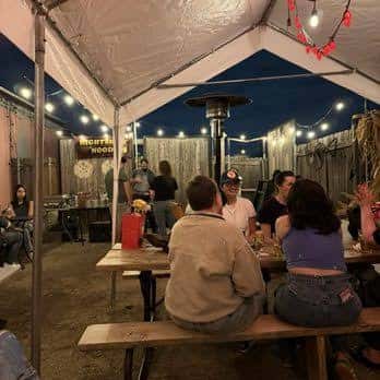 Área exterior cubierta con mesas de picnic y personas socializando
