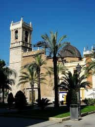 Plaza con palmeras y campanario histórico en el fondo, mostrando el entorno cultural de Valencia