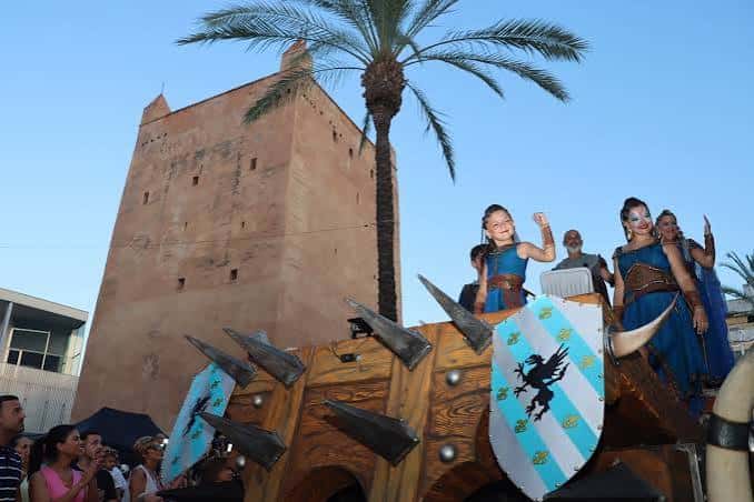 Carro alegórico con participantes vestidos de moros y cristianos frente a la Torre de Torrent