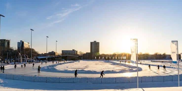 Pista de hielo del Emera Oval al atardecer con patinadores disfrutando del invierno