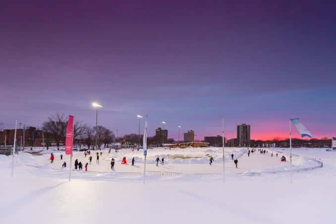 Emera Oval iluminado al anochecer con cielo violeta y personas patinando
