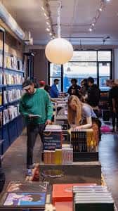 Interior de la librería TOMO MAGS mostrando estanterías azules, clientes navegando y una gran lámpara de papel colgante