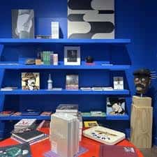 Detalle de una estantería azul con revistas de diseño y libros expuestos sobre una mesa roja